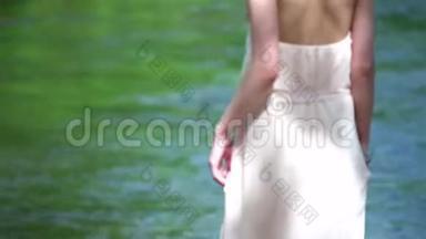 美丽的金发女孩，头上戴着一件连衣裙和花圈，走向河边。 新娘，婚礼日